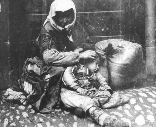 An Armenian woman and her child sit on a sidewalk next to a bundle of their possessions. Ottoman Empire - 1918-20 | Armenian Genocide | NewsComWorld.com